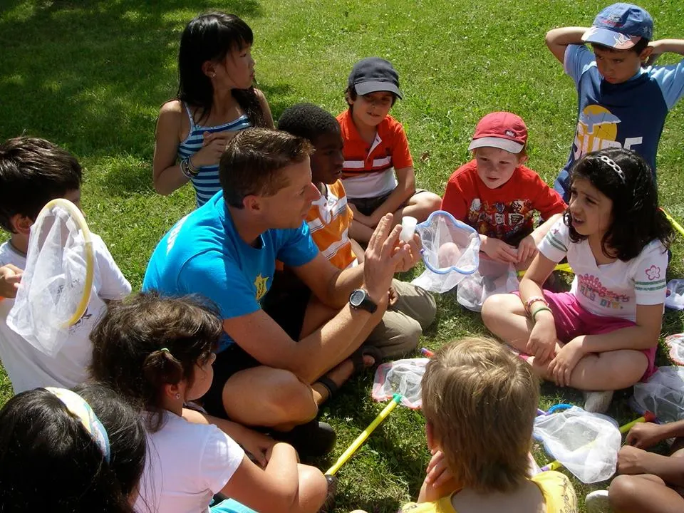 Des enfants assis dans l’herbe autour d’un animateur pendant une activité en plein air